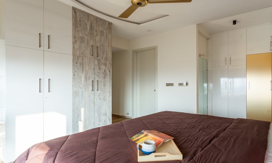 2 BHK house wardrobe in a white laminate and light wood finish in the guest room