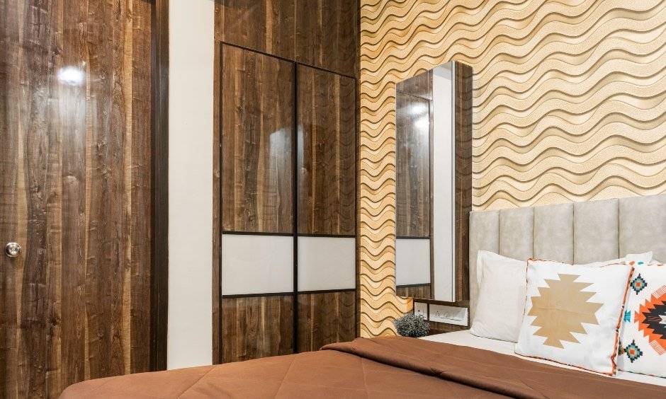 Earthy 2BHK bedroom with textured brown wall & wood laminate wardrobe with lofts for storage