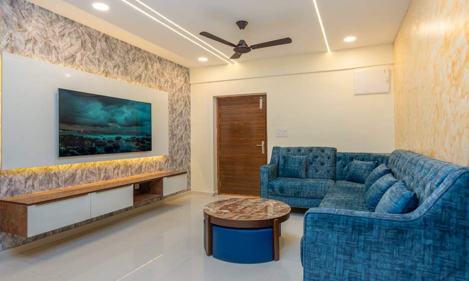 Minimalist living room in Nizampet, Hyderabad, with teal L-shaped sofa and sleek TV unit.