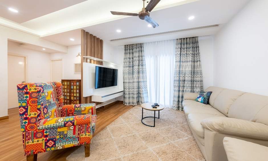 Cosy 3bhk living room in Bommanahalli showcases wall-mounted TV unit against wooden panelled backdrop